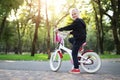 Cute adorable beautiful caucasian little blond girl enjoy riding white small bicycle by path in green summer city park Royalty Free Stock Photo