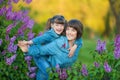 Cute adorable beautifull mother lady mom woman with brunette girl daughter in meadow of lilac purple bush.People in jeans wear. Royalty Free Stock Photo