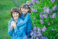 Cute adorable beautifull mother lady mom woman with brunette girl daughter in meadow of lilac purple bush.People in jeans wear. Royalty Free Stock Photo