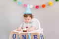 Cute adorable Caucasian baby boy in blue hat celebrating his first birthday at home. Child kid toddler sitting in high chair Royalty Free Stock Photo