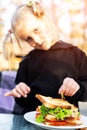 Cute adorable caucasian blond kid girl enjoy eating hamburger with ham and fresh vegeatables at cafe on bright sunny day outdoors Royalty Free Stock Photo
