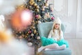 Cute adorable caucasian blond little kid girl sitting in chair at home near christmas tree and dreaming of christmas Royalty Free Stock Photo