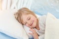 Cute adorable caucasian blond little toddler girl lying in bed on white pillow. Portrait of small beautiful long haired happy baby Royalty Free Stock Photo