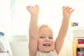 Cute adorable caucasian blond toddler boy having fun, laughing and rising hands up indoors. Cheerful child playing with positive Royalty Free Stock Photo