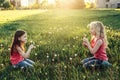 Cute adorable Caucasian girls blowing dandelions. Kiids sitting in grass on meadow. Outdoors fun summer seasonal children activity