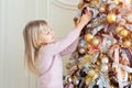 Cute adorable caucasian little blond smiling girl enjoy decorating christmas tree at home indoors. Happy child wearing pink Royalty Free Stock Photo