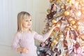 Cute adorable caucasian little blond smiling girl enjoy decorating christmas tree at home indoors. Happy child wearing pink Royalty Free Stock Photo