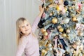 Cute adorable caucasian little blond smiling girl enjoy decorating christmas tree at home indoors. Happy child wearing pink Royalty Free Stock Photo