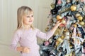 Cute adorable caucasian little blond smiling girl enjoy decorating christmas tree at home indoors. Happy child wearing pink Royalty Free Stock Photo
