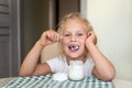 Cute adorable caucasian little funny blond girl eating yogurt or milk cottage cheese for lunch snack. Child enjoy eating