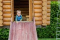 Cute adorable caucasian toddler boy having fun sliding down wooden slide at eco-friendly natural playground at backyard in autumn