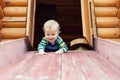 Cute adorable caucasian toddler boy having fun sliding down wooden slide at eco-friendly natural playground at backyard in autumn Royalty Free Stock Photo