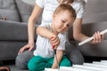 Cute adorable concentrated caucasian toddler boy kid sit on floor and help mom assembling furniture shelf with