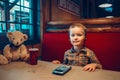 Cute adorable funny little boy toddler playing digital toy cell phone gadget with ear phones in a restaurant. Child using new Royalty Free Stock Photo