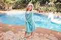 Cute adorable girl with freckles wrapped in beach towel standing by pool. Smiling funny child having fun in swimming pool. Summer Royalty Free Stock Photo