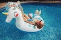 Cute adorable girl in sunglasses with drink lying on inflatable ring unicorn. Kid child enjoying having fun relaxing resting in Royalty Free Stock Photo