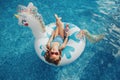 Cute adorable girl in sunglasses with drink lying on inflatable ring unicorn. Kid child enjoying having fun in swimming pool. Royalty Free Stock Photo