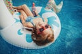 Cute adorable girl in sunglasses with drink lying on inflatable ring unicorn. Kid child enjoying having fun in swimming pool. Royalty Free Stock Photo