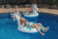 Cute adorable girls sisters friends with drinks lying on inflatable rings unicorns. Kids children siblings enjoying having fun in