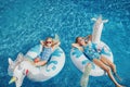 Cute adorable girls sisters friends with drinks lying on inflatable rings unicorns. Kids children siblings in sunglasses having