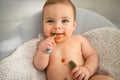 Cute adorable infant funny dirty baby trying to eat himself with fruit or vegetable puree smeared on his face. Baby Royalty Free Stock Photo