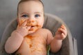 Cute adorable infant funny dirty baby trying to eat himself with fruit or vegetable puree smeared on his face. Baby Royalty Free Stock Photo
