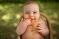 Cute adorable infant funny dirty baby trying to eat himself with fruit or vegetable puree smeared on his face. Baby Royalty Free Stock Photo