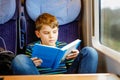 Cute adorable kid boy reading book during traveling by train. Happy child sitting near window. Family going on vacations Royalty Free Stock Photo