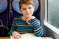 Cute adorable kid boy reading book during traveling by train. Happy child sitting near window. Family going on vacations Royalty Free Stock Photo
