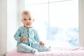 Cute adorable little baby girl sitting by window and looking to cam. Kid enjoy snowfall. Happy holidays and Christmas! Winter Home Royalty Free Stock Photo