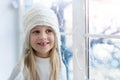 Cute adorable little blond beautiful cauasian girl stay near window, dream and looking outside waiting for snow, wonders