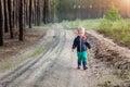 Cute adorable little blond caucasian toddler boy walking alone by rural country sand road on ranch or farm at coniferous Royalty Free Stock Photo