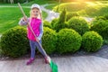 Cute adorable little caucasian girl hepling parents sweeping yard with broom on warm bright autumn evening outdoors Royalty Free Stock Photo