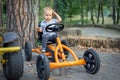 Cute adorable pensive caucasian toddler boy sitting at pedal toy car and wondering how to drive it outdoors in city park, garden