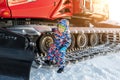 Cute adorable playful happy toddler boy play at red modern snowcat ratrack snowplow box grooming standing on peak alpine Royalty Free Stock Photo