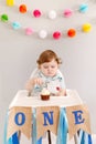 Cute adorable sad upset Caucasian baby boy celebrating first birthday at home. Pensive child kid toddler sitting in high chair Royalty Free Stock Photo