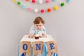 Cute adorable sad upset Caucasian baby boy celebrating his first birthday at home. Pensive child kid toddler sitting in high chair