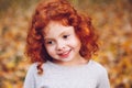 Cute adorable smiling little red-haired Caucasian girl child standing in autumn fall park outside, looking away Royalty Free Stock Photo
