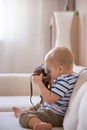 Cute adorable toddler boy sitting on the sofa in the living room and playing with vintage photo camera. Child taking picture with Royalty Free Stock Photo