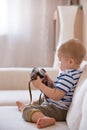 Cute adorable toddler boy sitting on the sofa in the living room and playing with vintage photo camera. Child taking picture with Royalty Free Stock Photo