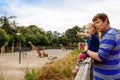 Cute adorable toddler girl and father watching and feeding giraffe in zoo. Happy baby child, daughter and dad, family