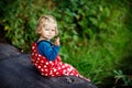 Cute adorable toddler girl sitting on wooden bridge and throwing small stones into a creek. Funny baby having fun with Royalty Free Stock Photo