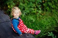 Cute adorable toddler girl sitting on wooden bridge and throwing small stones into a creek. Funny baby having fun with Royalty Free Stock Photo