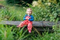 Cute adorable toddler girl sitting on wooden bridge and throwing small stones into a creek. Funny baby having fun with Royalty Free Stock Photo