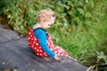 Cute adorable toddler girl sitting on wooden bridge and throwing small stones into a creek. Funny baby having fun with Royalty Free Stock Photo