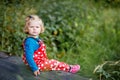 Cute adorable toddler girl sitting on wooden bridge and throwing small stones into a creek. Funny baby having fun with Royalty Free Stock Photo