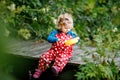 Cute adorable toddler girl sitting on wooden bridge and throwing small stones into a creek. Funny baby having fun with Royalty Free Stock Photo