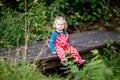 Cute adorable toddler girl sitting on wooden bridge and throwing small stones into a creek. Funny baby having fun with Royalty Free Stock Photo