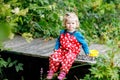 Cute adorable toddler girl sitting on wooden bridge and throwing small stones into a creek. Funny baby having fun with Royalty Free Stock Photo