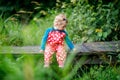 Cute adorable toddler girl sitting on wooden bridge and throwing small stones into a creek. Funny baby having fun with Royalty Free Stock Photo